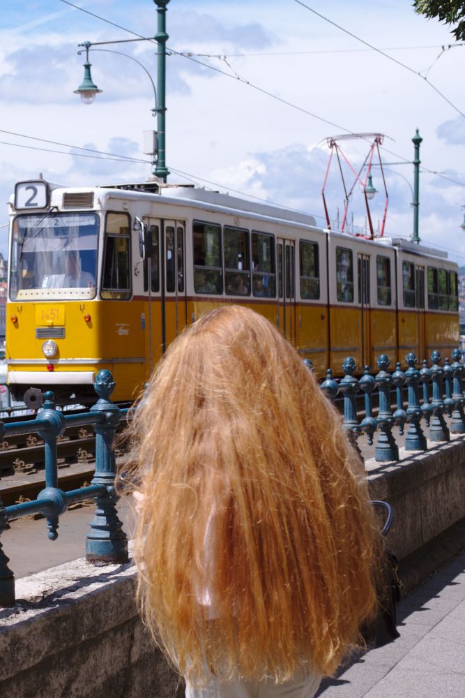 A red haired person in front of a yellow tramway in Budapest