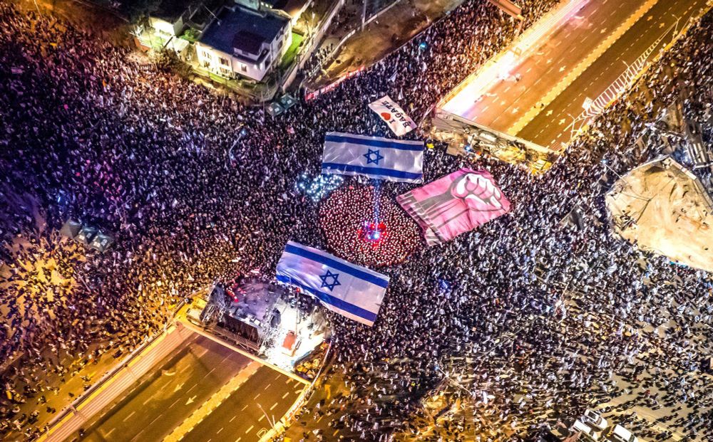 Aerial image of a crowd - it's half a million Israelis protesting in 2023 against proposed judicial reforms that would have granted Netenyahu absolute legal immunity and power to overturn high court rulings. 
