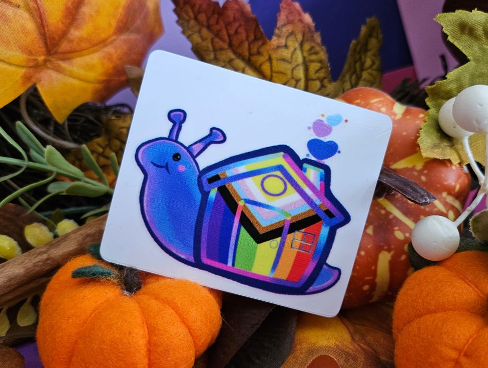 A transparent window sticker on its white backer. The image is a blue/purple cartoon snail with a house shaped shell that is painted in the colours of the intersex inclusive progressive pride flag.