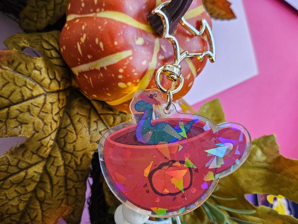 An acrylic keychain of an orange teacup with nessie swimming in it