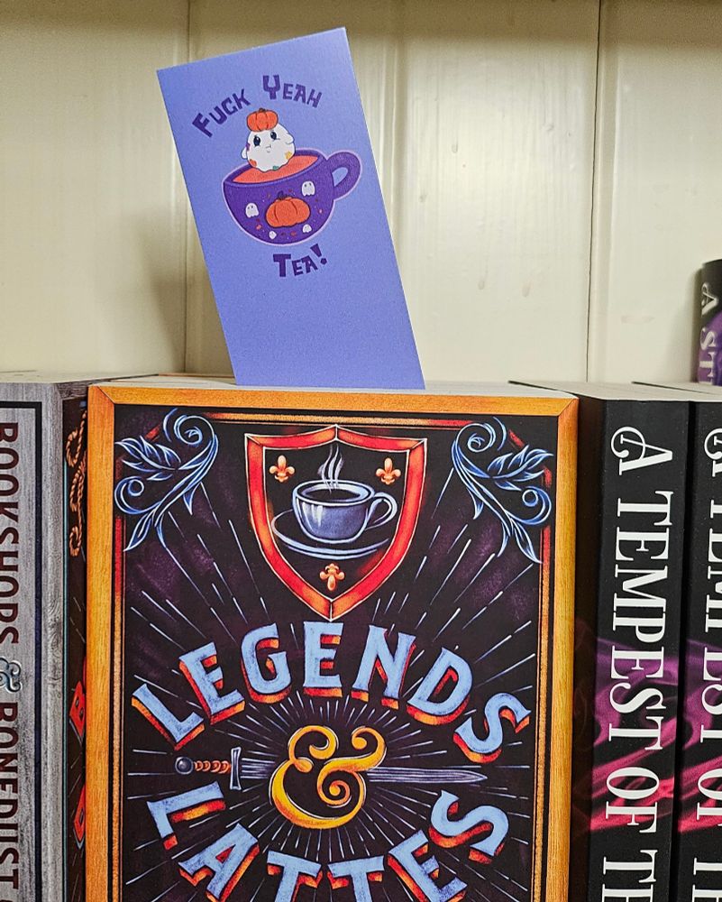 A light purple bookmark that has a little illustration of a ghost who has a pumpkin on their head and is hovering above a pumpkin spice tea cup and around them is the caption "Fuck Yeah Tea!"