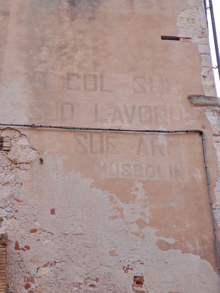 Texte peint sur un mur, en partie effacé par le temps, et signé Mussolini. Photo prise a Cagliari (Sardaigne) en mai 2025.