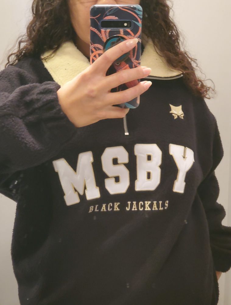 A mirror selfie of me wearing fan produced merch. It's a quarter zip pullover, black with a gold collar, and on the front it says MSBY Black Jackals