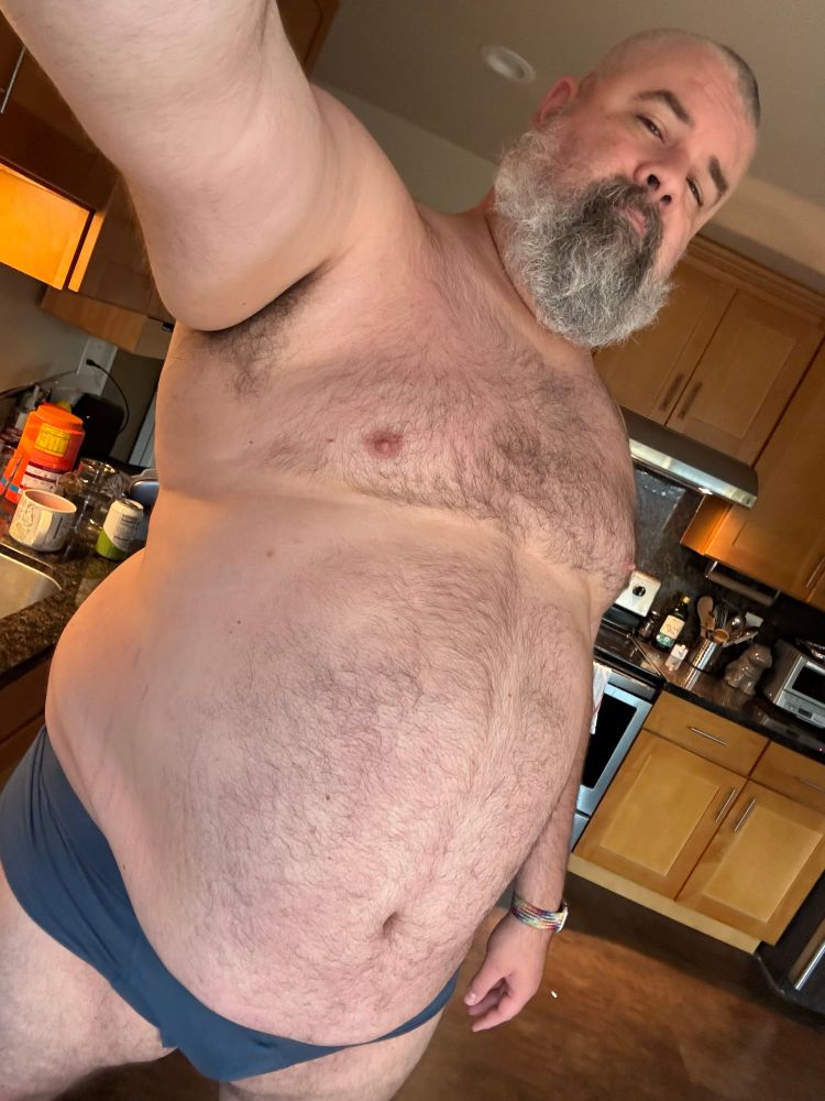 A picture of a fat man with a great beard wearing only navy blue briefs, taking a selfie in the kitchen. He has strategically angled the camera to make his large belly the focus of this photograph in keeping it with the customs and traditions of tummy Tuesday.