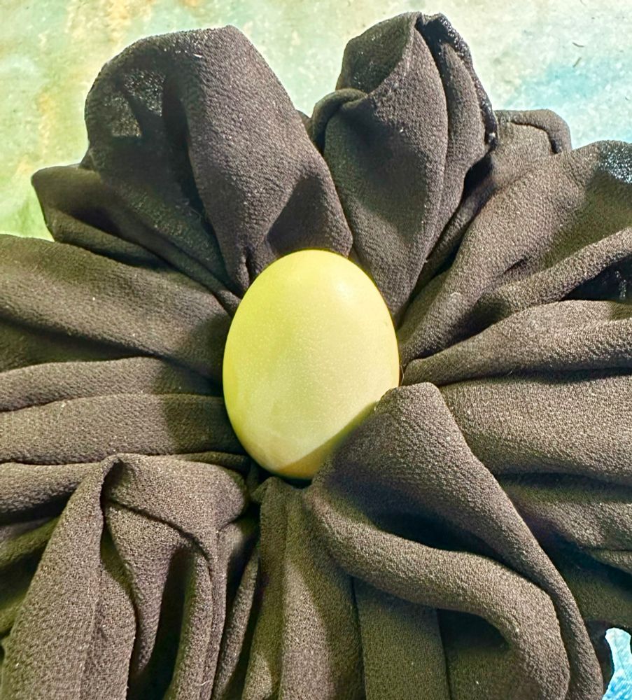 A la all light green egg in a giant black scrunchie on a desk