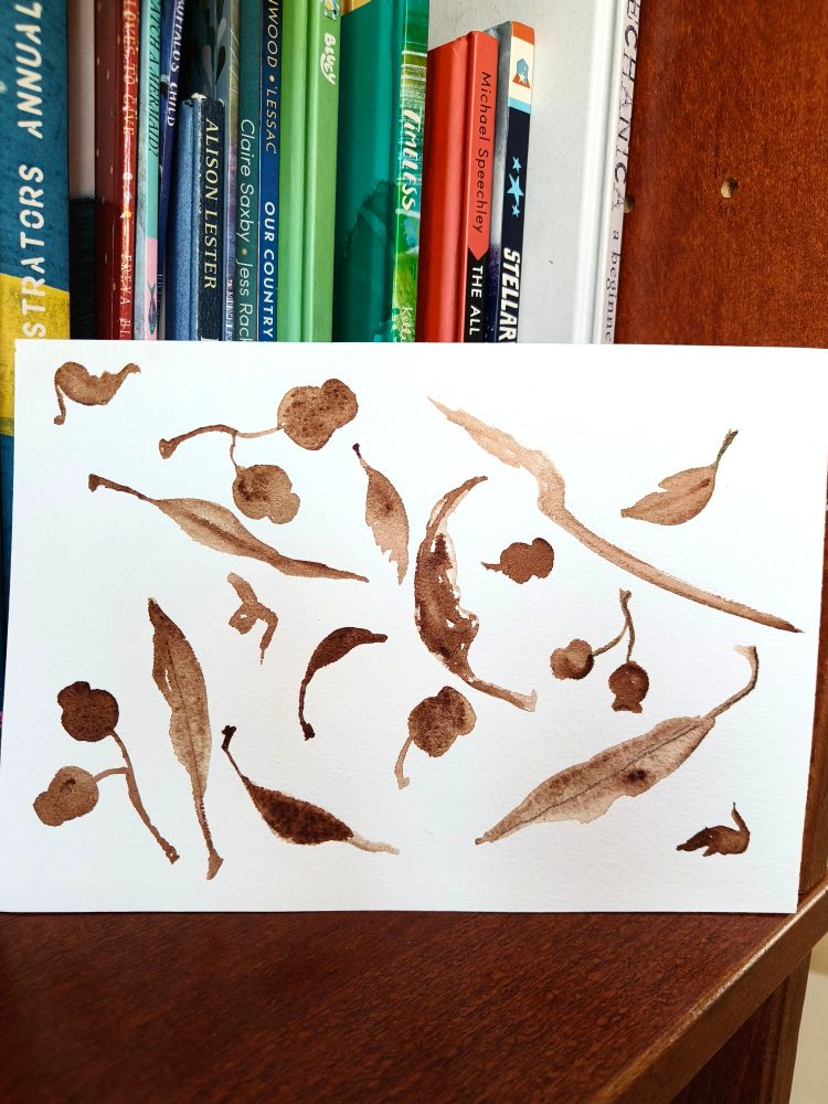 A photo of a piece of art on a book shelf. Leaves and gumnuts are painted in burnt sienna 