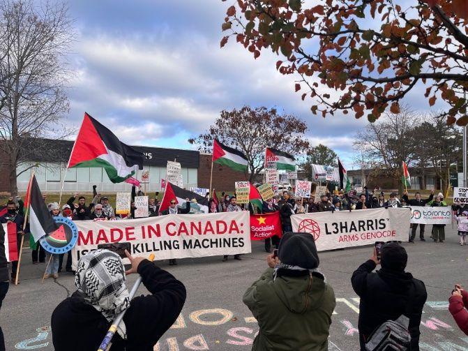 Photo of a pro-Palestine protest with lots of Palestinian flags flying and people holding banners that read:
MADE IN CANADA
ISRAEL'S KILLING MACHINES

L3HARRIS
ARMS GENOCIDE

STOP THE GENOCIDE