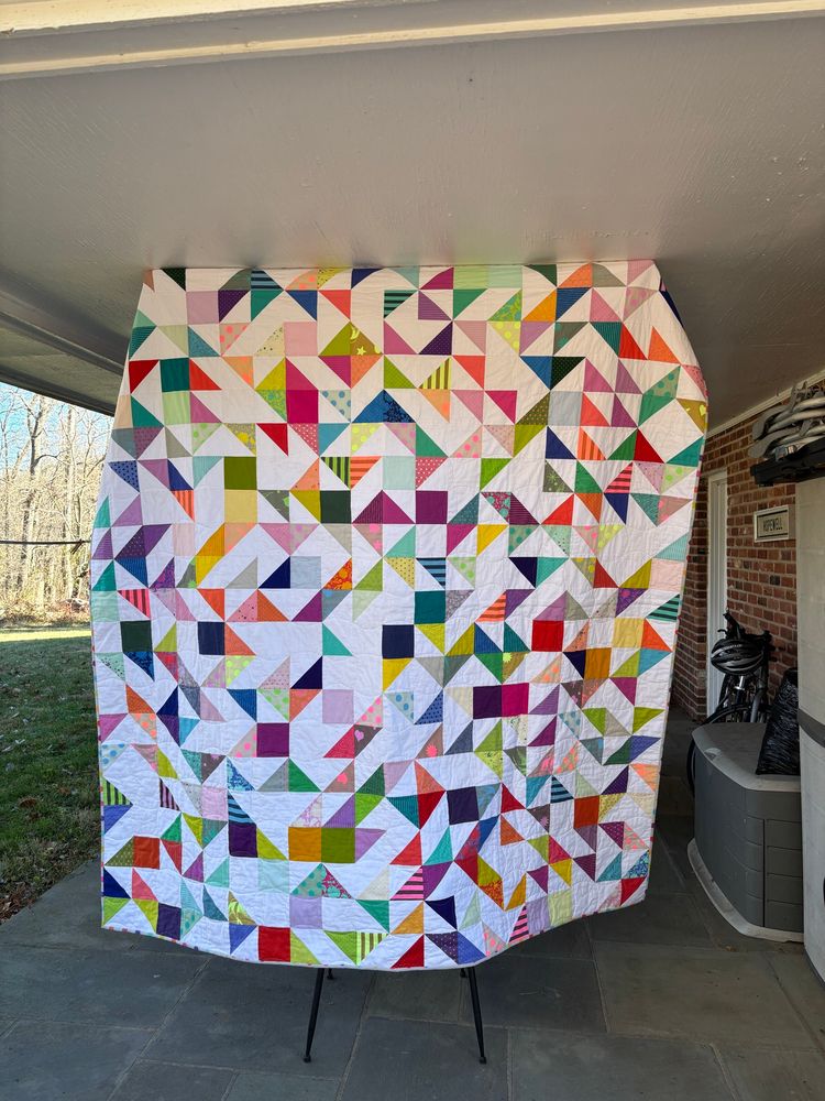a quilt made of colorful triangles and squares mixed with white triangles and squares in a random pattern.