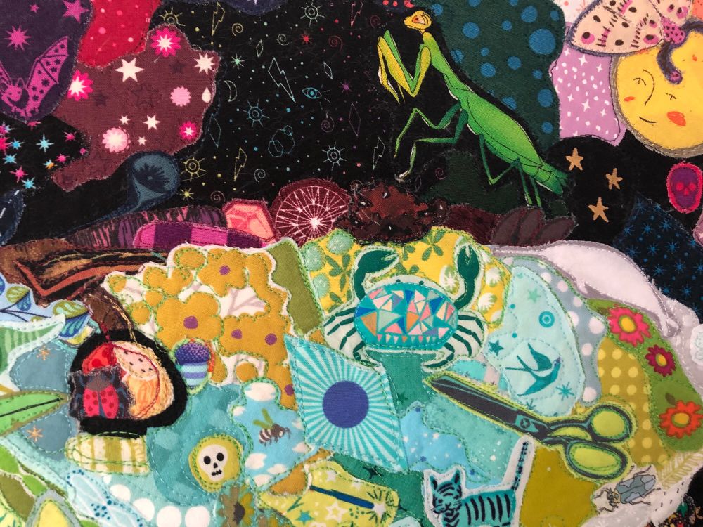 detail shot of a maximalist appliqué quilt of a luna moth made of hundreds of small pieces of fabric. the motifs used include skulls, crabs, other insects, cats, stars, erasers, flowers, scissors, and lots of other things