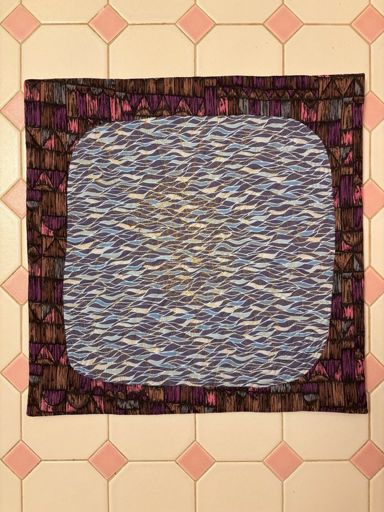 the back of the quilt with a facing. the back is a blue sort of wavy watery print. the facing is a wooden sort of print in brown, purple, and pink. it frames the backing fabric and makes it look like an old tv tuned to static. where is william gibson.