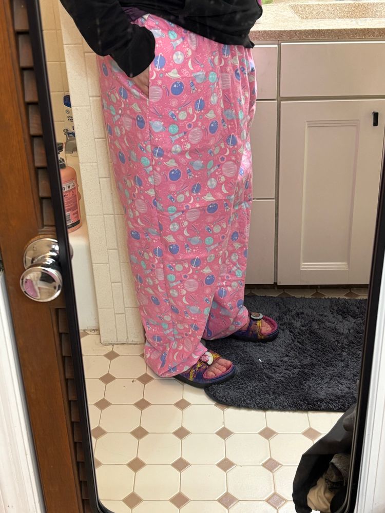 mirror picture of me wearing very loose flannel lounge pants. the fabric is pink with planets and spaceships printed on it.