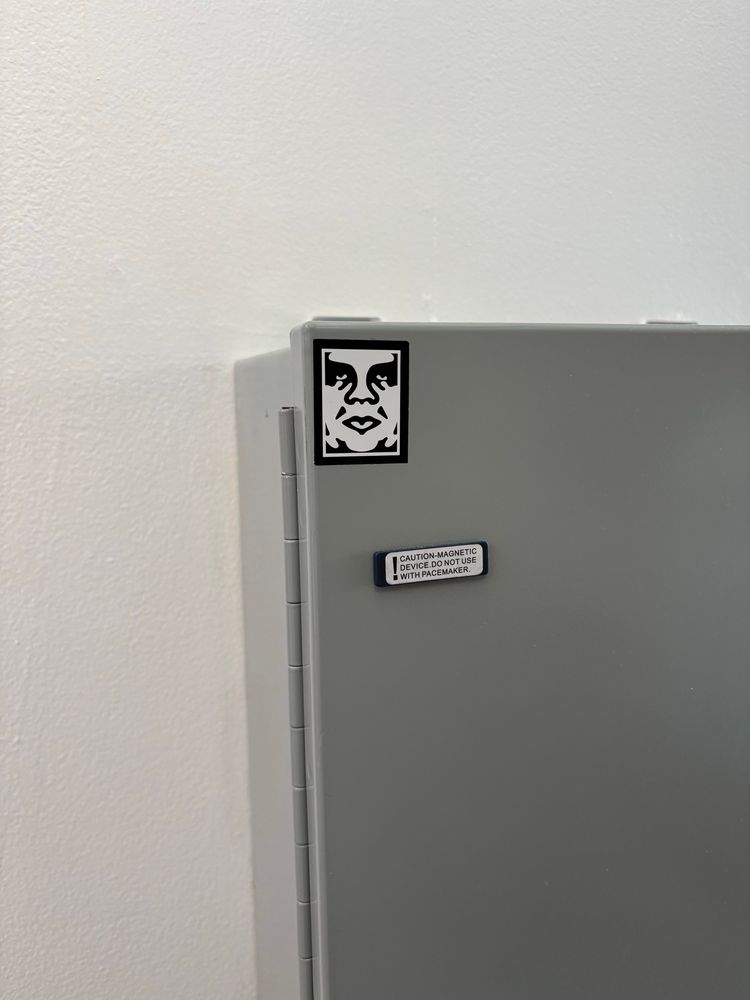 a metal box mounted on the wall with a small obey giant sticker by shepard fairey. it’s a black and white rendering of andre the giant’s face. also there’s a little label that says CAUTION-MAGNETIC DEVICE. DO NOT USE WITH PACEMAKER.