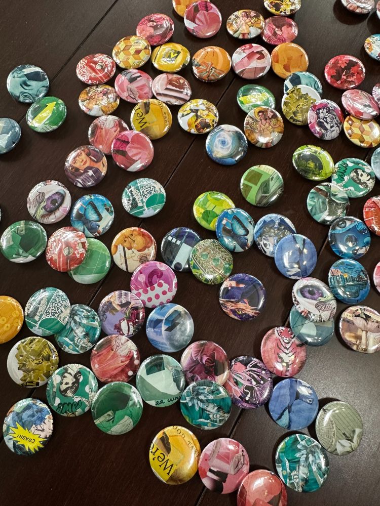 A bunch of 1-inch buttons scattered on a dark wood floor. The buttons feature colorful collage artwork.