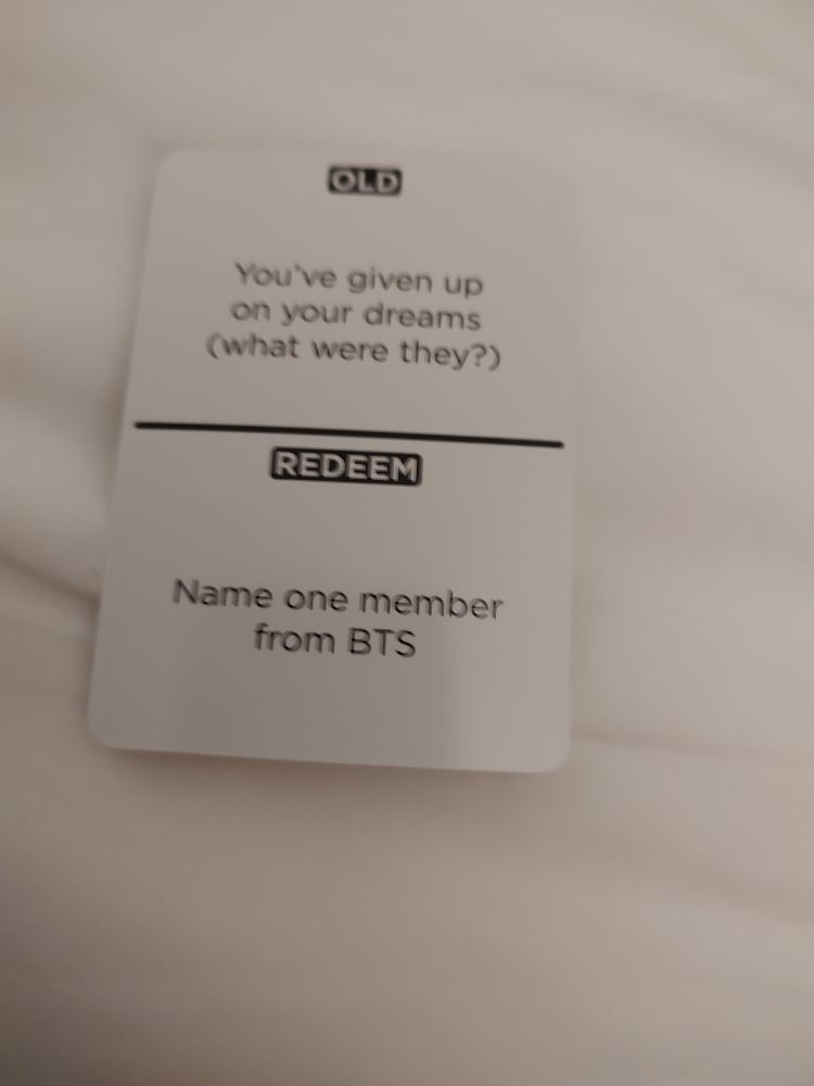 A photo of a game card that reads "OLD - You've given up on your dreams (what were they?) . . . REDEEM Name one member from BTS."