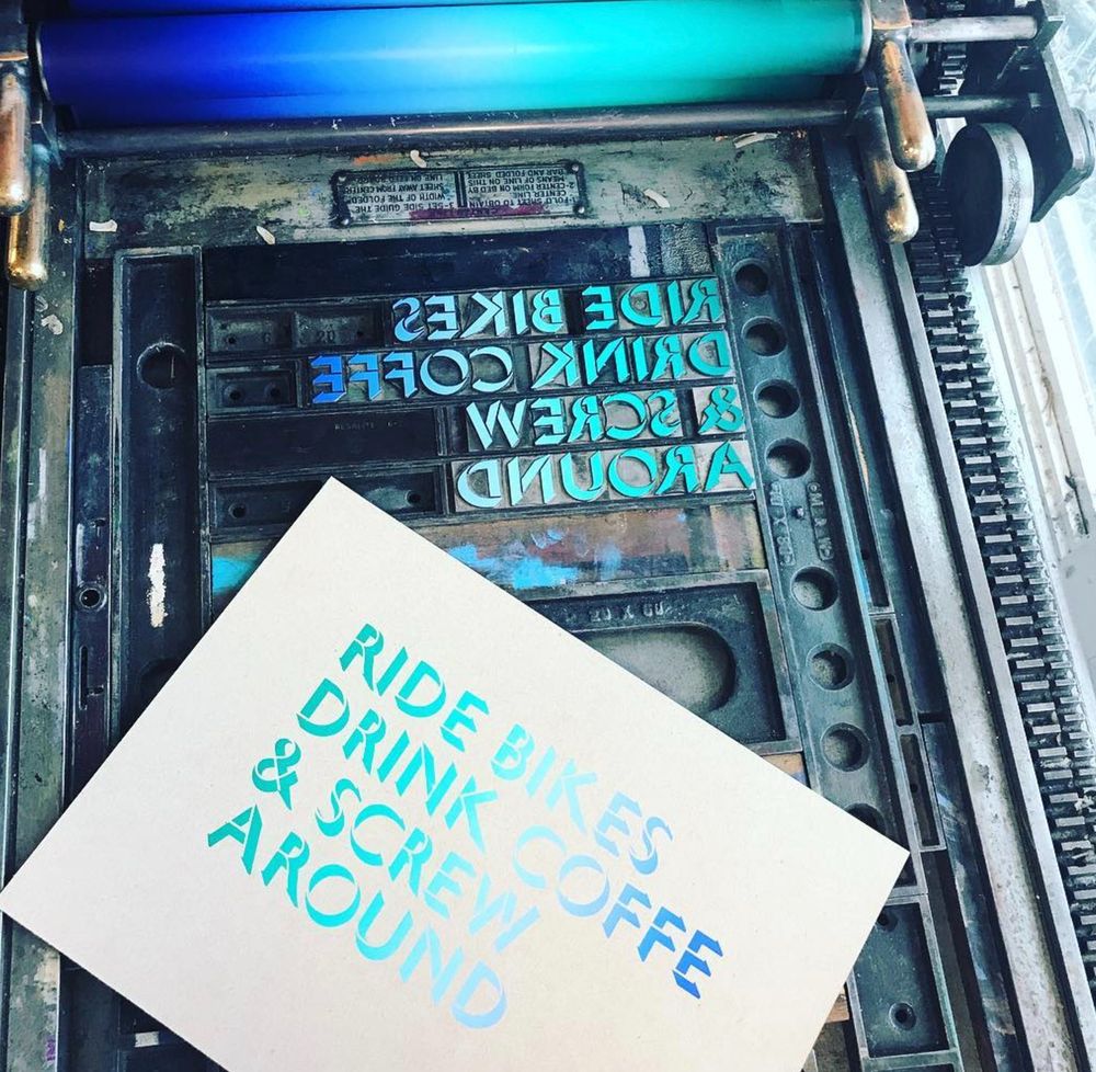 A test Letterpress print on brown card stock reads, "Ride Bikes, Drink Coffe & Screw Around". The word coffee is unintentionally misspelled, with only one e. 