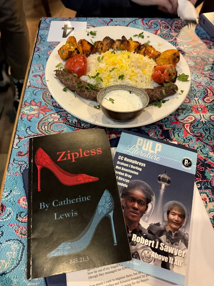 A copy of my chapbook ZIPLESS and of Pulp Literature’s Issue 40 sit on a patterned table next to a mixed-kebab platter.