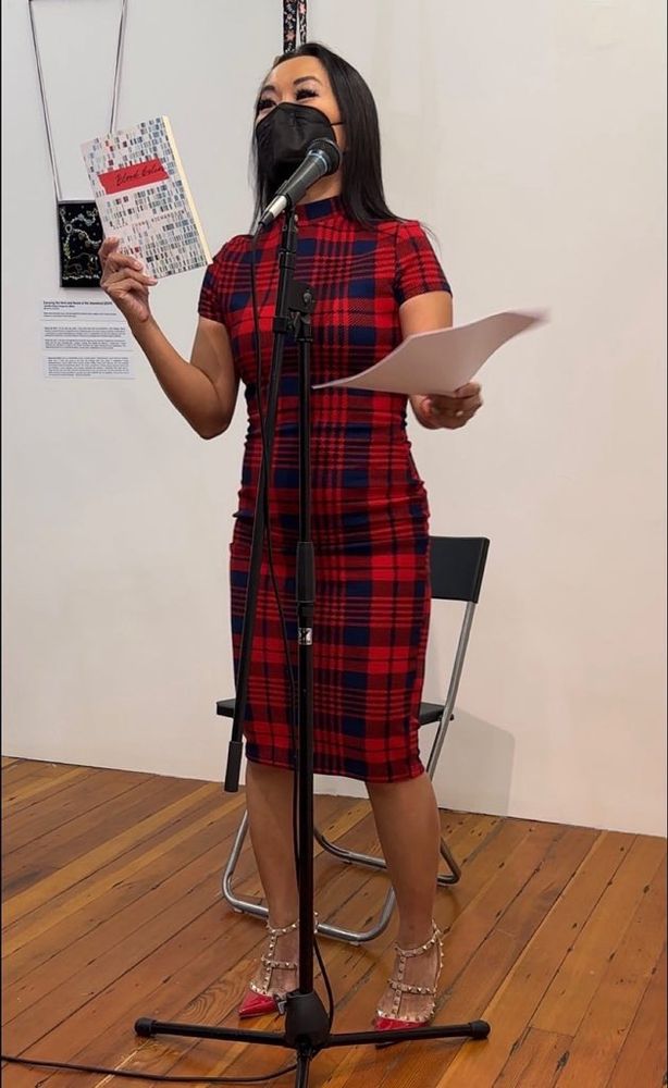 Catherine Lewis up at the mic, holding a copy of Ellen Chang-Richardson’s book BLOOD BELIES