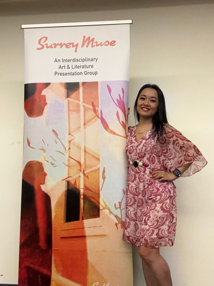 Catherine Lewis standing next to a banner with the text “Surrey Muse: An Interdisciplinary Art & Literature Presentation Group”