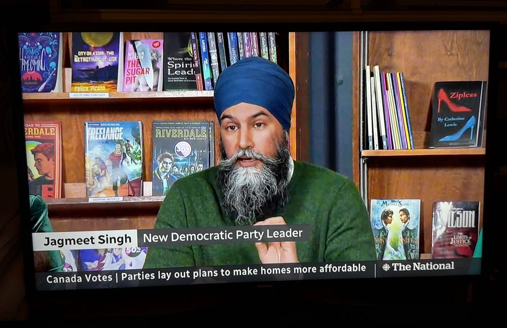 On The National, New Democratic Party Leader Jagmeet Singh is seated in front of bookshelves. ZIPLESS is displayed on a shelf behind Singh’s left shoulder.
