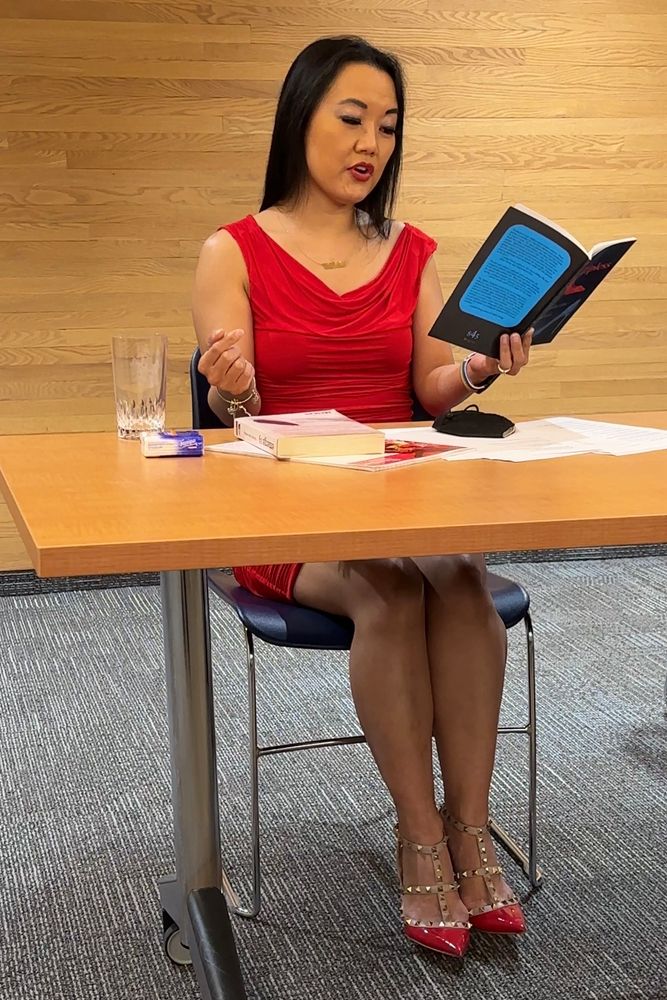 Catherine Lewis reading from her chapbook ZIPLESS while seated behind a long table