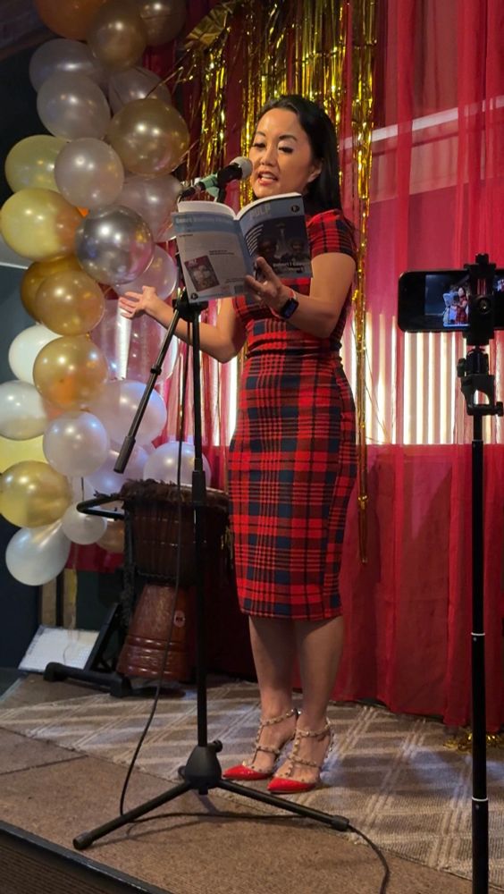 Catherine Lewis up at the mic in a red and black dress, reading from
Issue 40 of Pulp Literature.