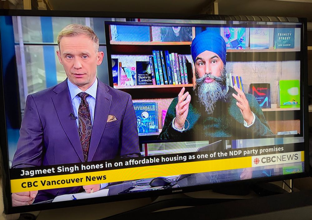CBC Vancouver News anchor Dan Burritt presenting segment about NDP Leader Jagmeet Singh, who is seated in front of bookshelves. ZIPLESS is displayed on a shelf behind Singh’s left shoulder.