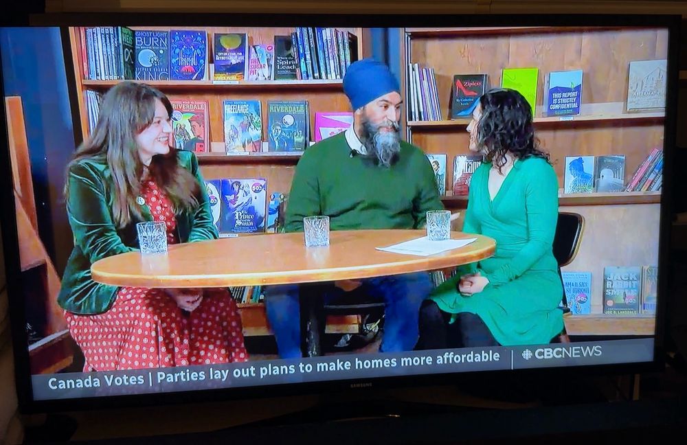 On CBC News, NDP Leader Jagmeet Singh and two other individuals are seated at a round table, in front of bookshelves. ZIPLESS is displayed on a shelf behind Singh’s left shoulder.