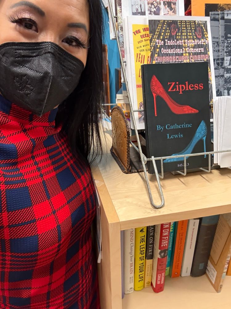 Catherine Lewis in a tartan dress standing next to in-store display of her chapbook ZIPLESS