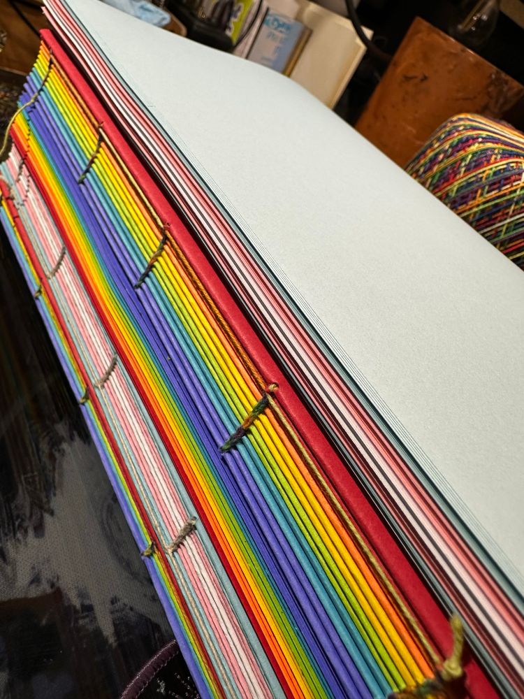 The spines of rainbow text blocks. Stitched and ready to go. Some are gay pride. Some re trans pride. 