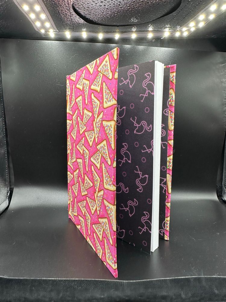 A book bound in a fabric featuring fairy bread on a pink background. The inside has flamingoes done in neon. 
