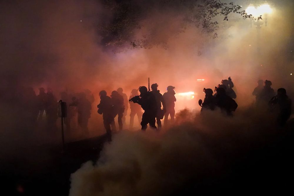 Picture at night of military in the enlightened smoke of tear gas. 
