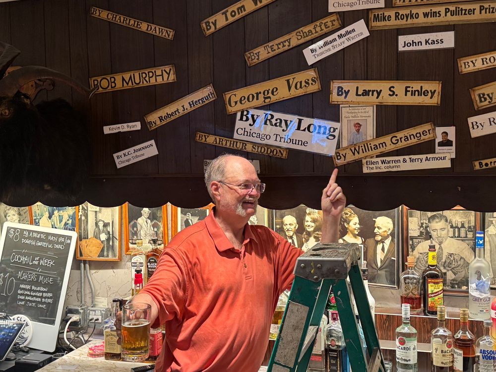 Ray Long holds a beer in one hand while pointing with his other hand at his byline on the Billy Goat’s wall of fame.