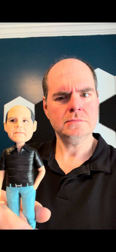 A man posing with a bobblehead that looks like him