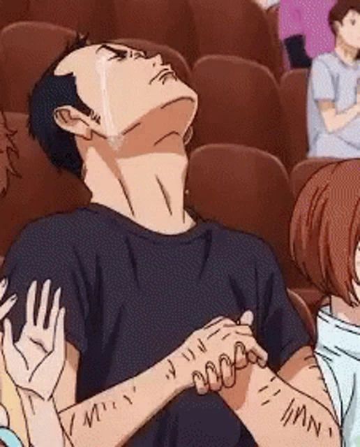 a man is crying while sitting in a theatre with his hands on his chest