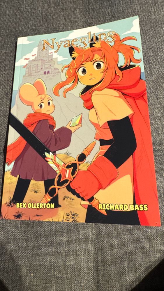 Book cover for graphic novel, Nyaegling. A catgirl holds a black sword with gold decorative metal and colourful crystals attached. Behind her is an NB mouse wearing a red scarf and purple shawl. Behind them is a castle and above them the title Nyaegling.  