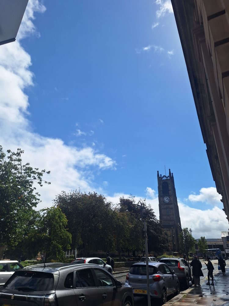 Blue skies and clouds, sun shining off very wet pavements just after a downpour in the centre of Huddersfield