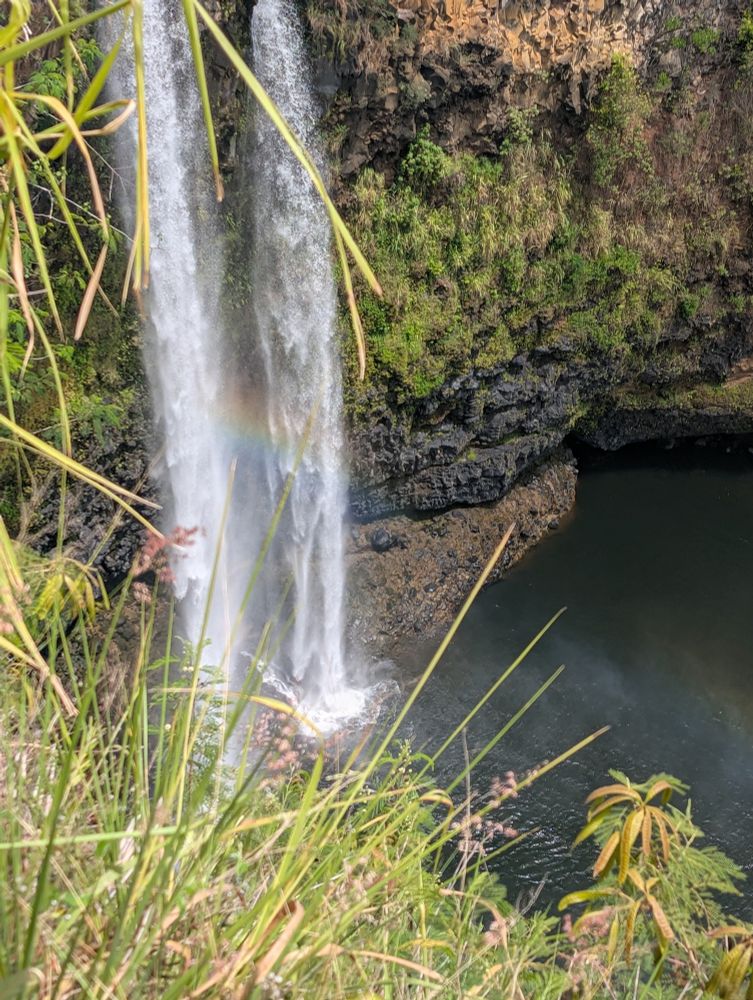 A waterfall with a rainbow shimmering between the streams falls into a grotto