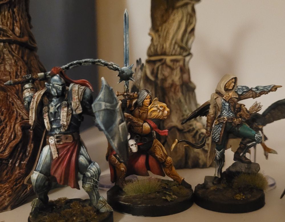 3 fantasy gaming figures painted. They are standing in front of some trees.