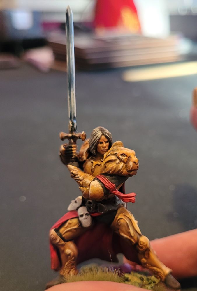 A painted miniature gaming figure in gold armor holding a sword 
