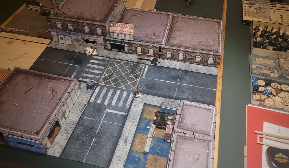 A tabletop game set up depicting a small town intersection with several commercial buildings.