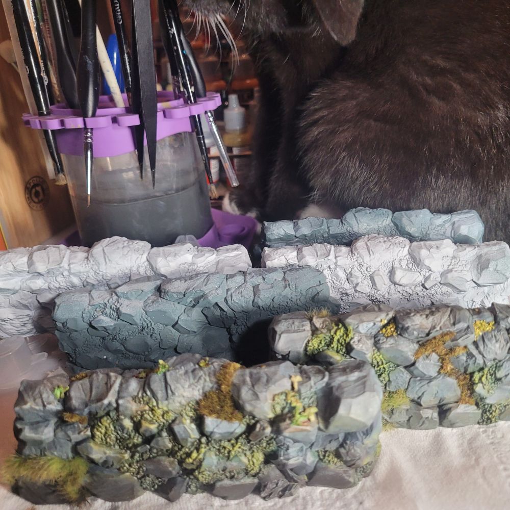 Tabletop gaming terrain. Stone walls with moss and vegetation growing on them. Cat for scale.