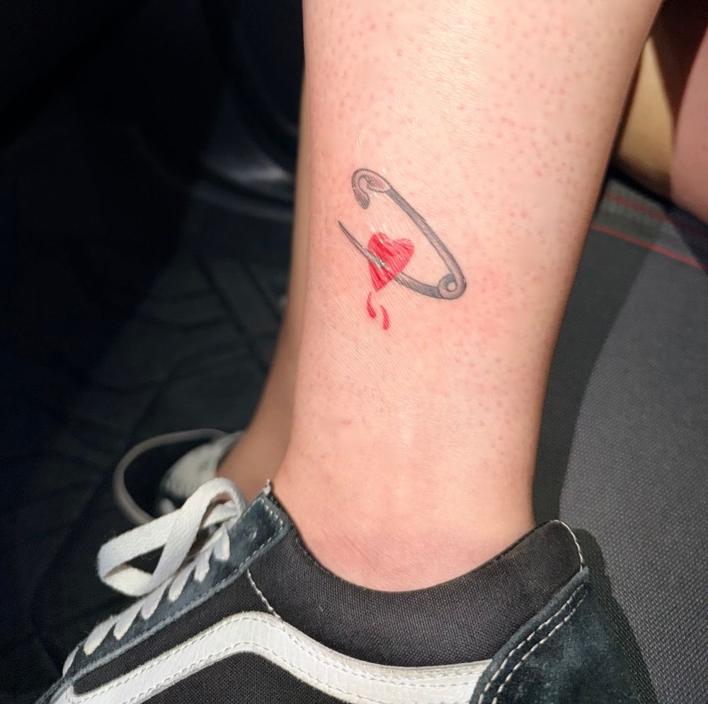 Slimes ankle with a little tattoo of a safety pin with a bloody little heart being stabbed and her vans