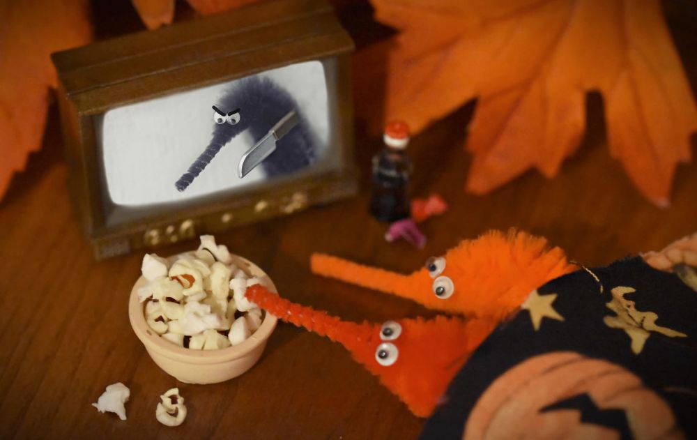 Two worm on a string with a little bowl of porcini laying under a blanket watching a movie with a murderous work on a string holding a knife 