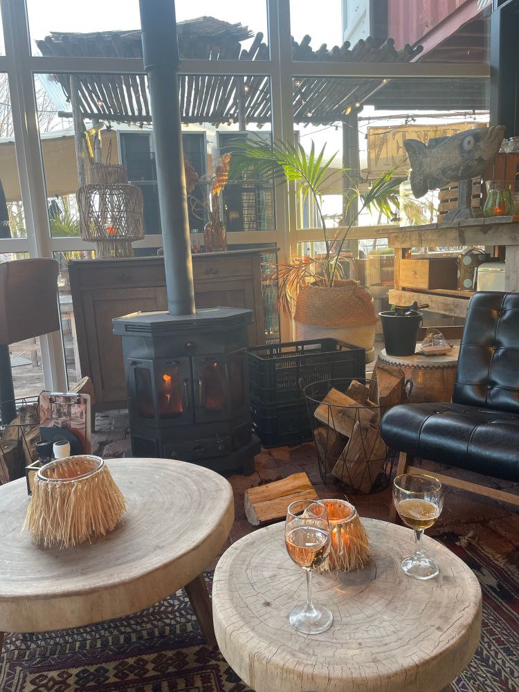 Rosé en bier op witte boomstam salontafel met zwarte leren stoel en brandende haard. 