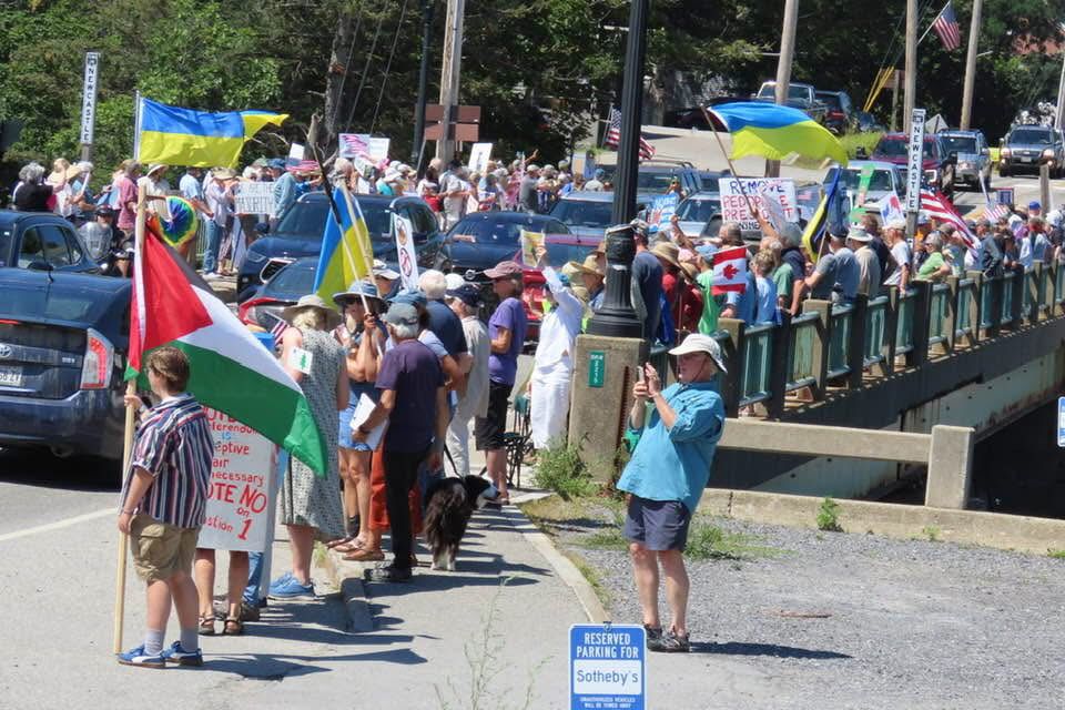 Large crowd of protesters gathered on the Newcastle Damariscotta Bridge. Ukrainian flags seem in the picture. 