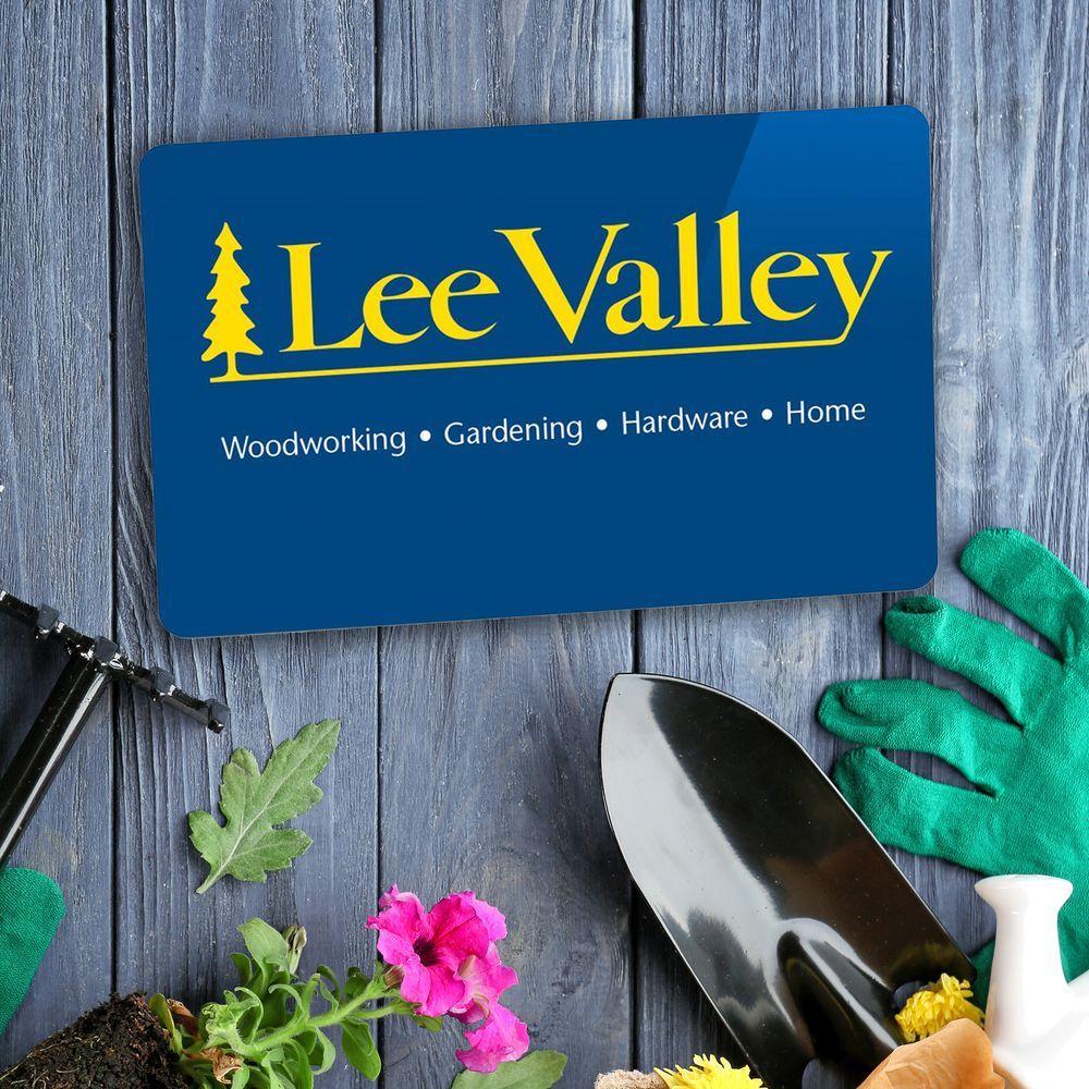 Blue Lee Valley gift card with the words woodworking, gardening, hardware, home under the yellow Lee Valley logo. The card is superimposed over a light blue table surface with gardening tools scattered across it.