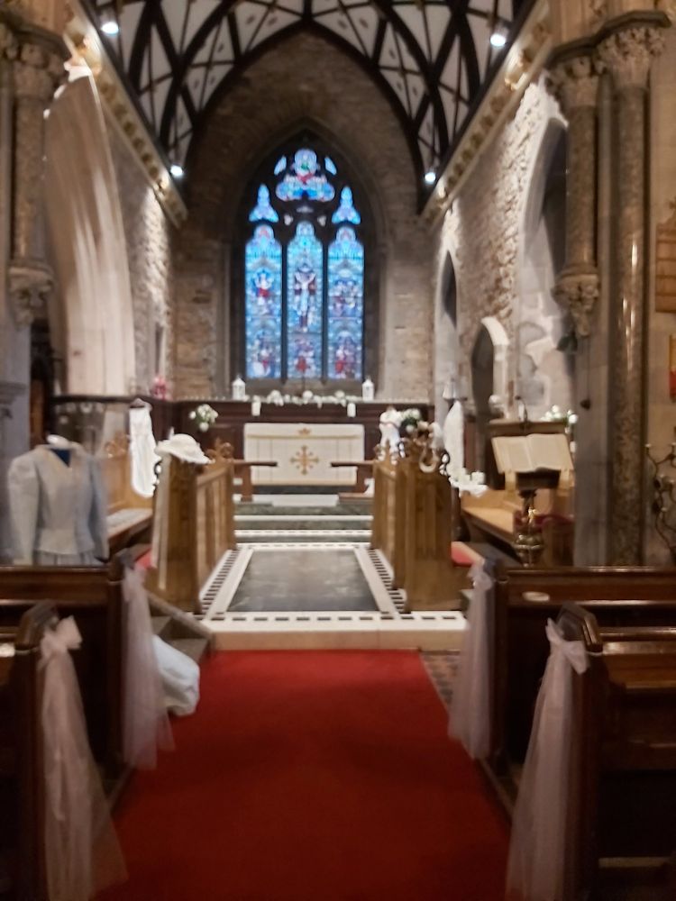 View to East window of church.
Red carpet down Central aisle
White candles and flowers at altar.
Wedding dresses on display.
The pale blue dress at the front left was made by the bride including all her own lace.
White bows on end of each pew.