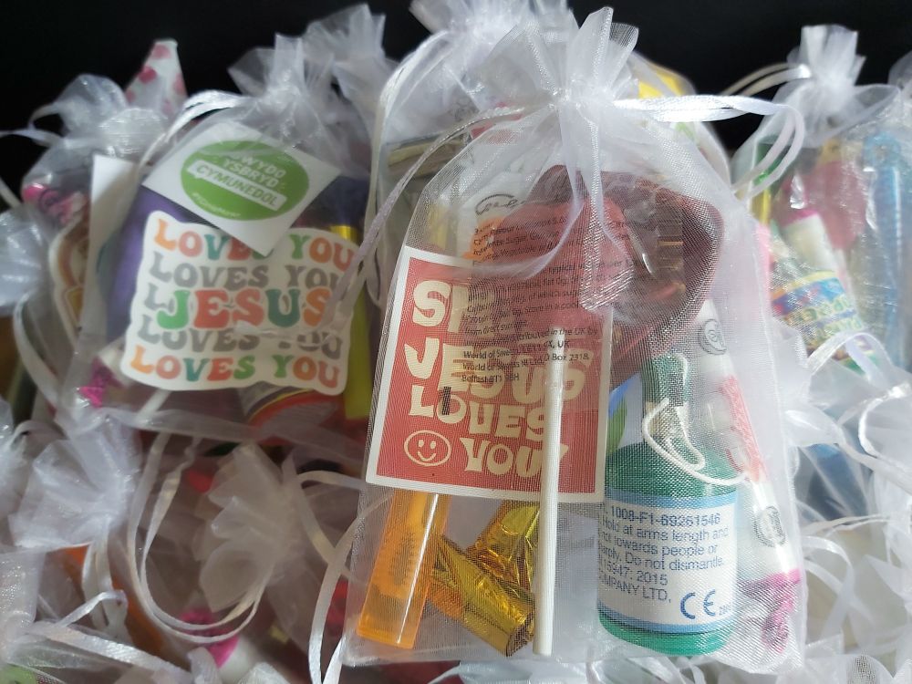 Goody bag for a child to have in service. 
White organza bag with party popper, heart lolly, bubbles, party blower, fizzy sweets, balloon and a smile Jesus loves you sticker