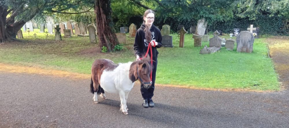 Teenager leading a tiny pony through a churchyard