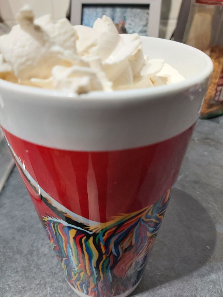 Tall red cup with a multi coloured cow on. Containing squirty cream